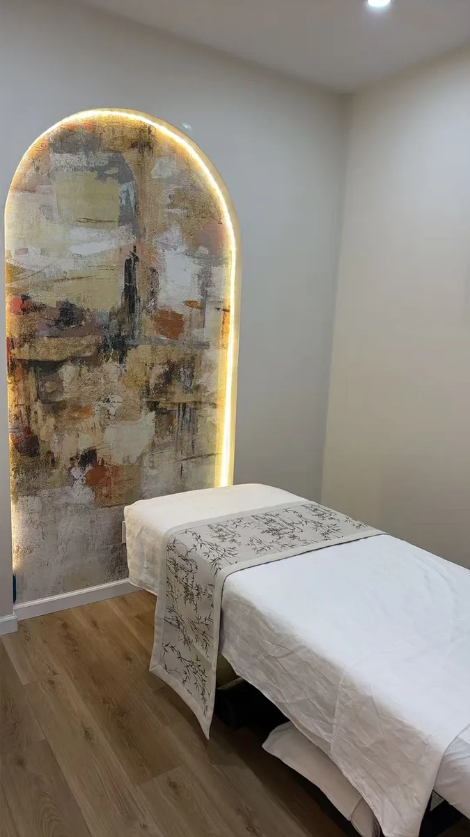 A treatment room with a tall arched art panel lit from behind, table made up